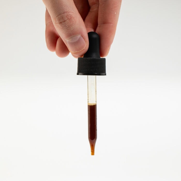 A one milliliter dropper-full of Skullcap glycerite held in front of a white background